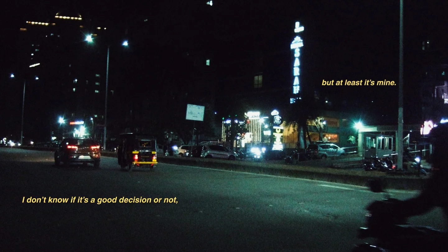 Traffic on a wide road at night under green street lights, with yellow subtitles