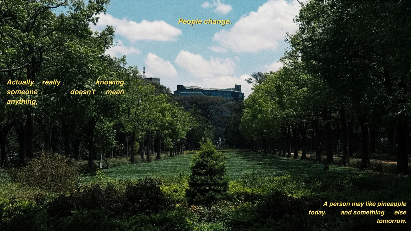 A tree-lined park under a bright sky, with yellow subtitles scattered over it